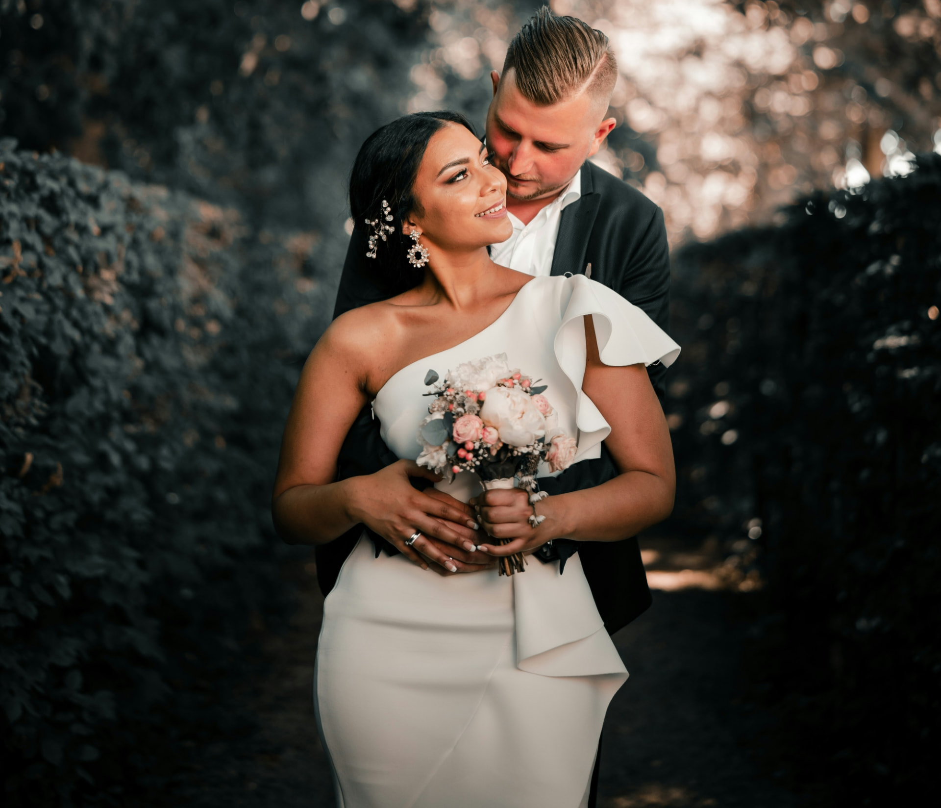 Mariés enlacés dans un parc, la mariée tenant son bouquet