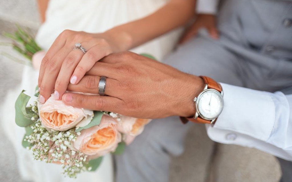 Mains d'un couple de mariés portant leurs alliances, avec un bouquet